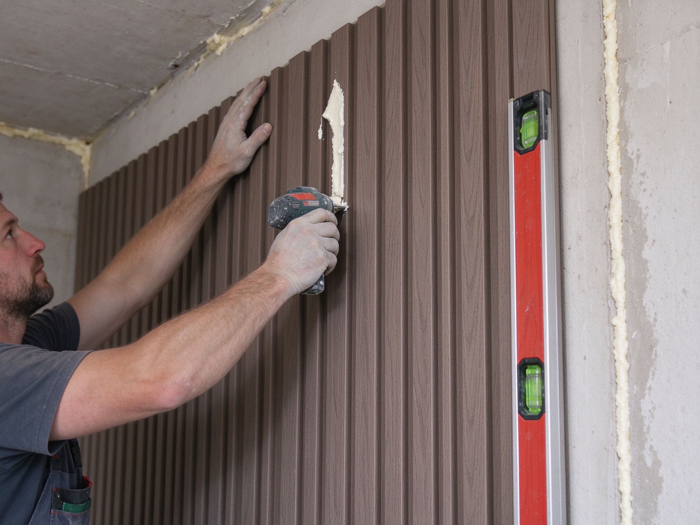 Installer fitting WPC fluted panel with adhesive and spirit level